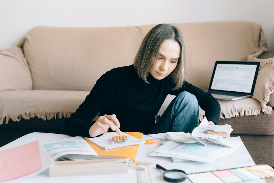 Young woman handling financial tasks with papers and laptop in cozy living room.