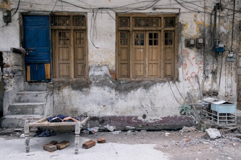 A rustic street scene in Faisalabad featuring weathered architecture and a charpoy bed.